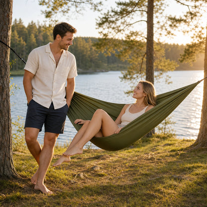 Couple relaxing beside a lake with an army-green double camping hammock